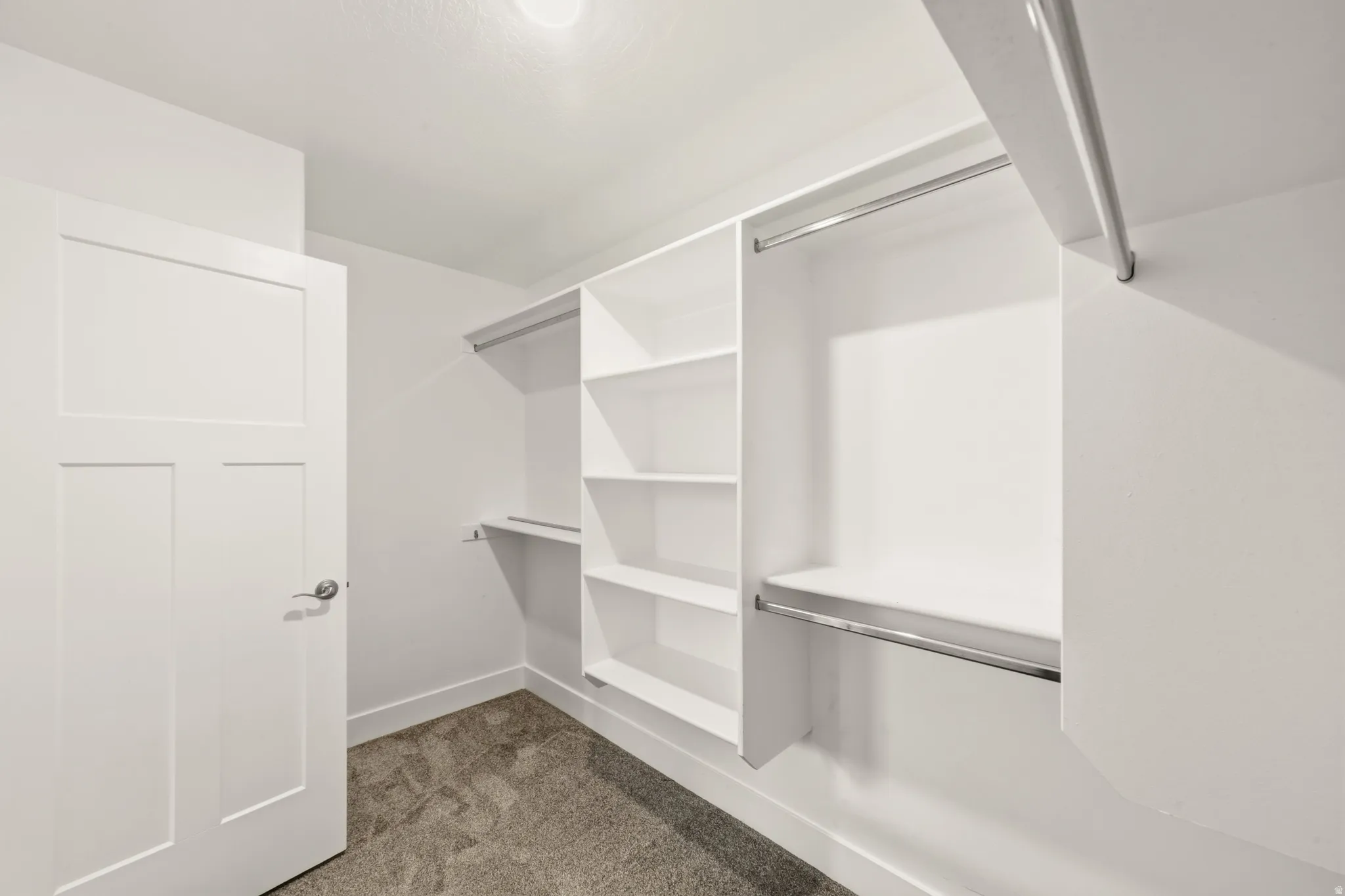 Walk-in closet featuring white built-in shelving, multiple hanging rods, and gray carpet flooring