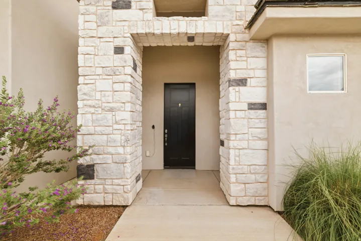 Stone facade entry with a dark panel door, stucco exterior, and square window
