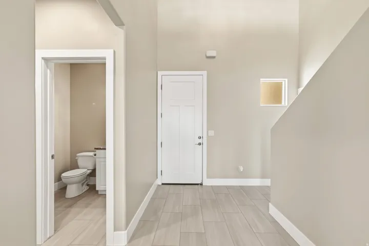 Entryway featuring wood-finish flooring, a contemporary white door, and a conveniently located powder room with a white vanity and toilet