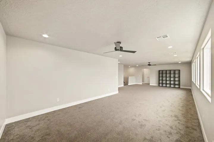 Expansive carpeted room featuring multiple windows, recessed lighting, and two ceiling fans
