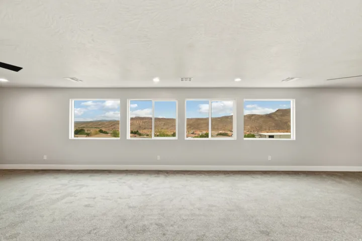 Spacious room featuring four large windows, grey wall paint, plush carpet flooring, and recessed ceiling lighting