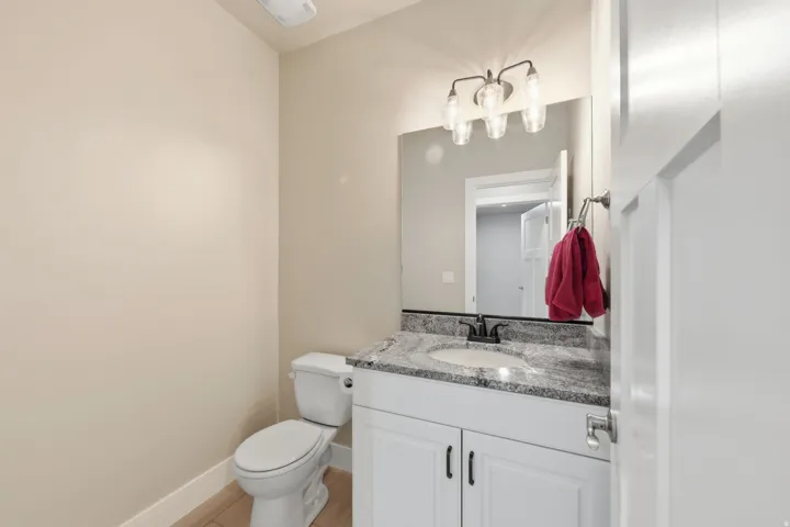 Bathroom with a white vanity featuring shaker-style cabinetry and dark hardware, a granite-finish countertop with an undermount sink, and a wall-mounted mirror