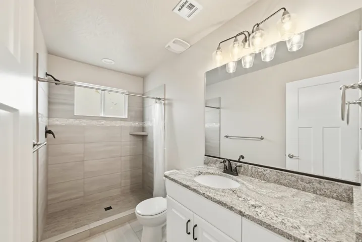 Bathroom featuring a walk-in shower with light grey tile surround, decorative mosaic tile accent, and built-in shelf