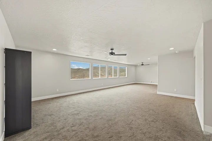 Spacious room featuring multiple horizontal windows, recessed lighting, two ceiling fans, gray carpeting, and baseboard molding