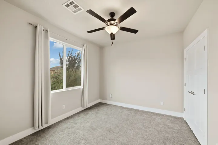 Spacious room featuring a large window, a ceiling fan with integrated lighting, neutral-toned walls, and grey carpeting