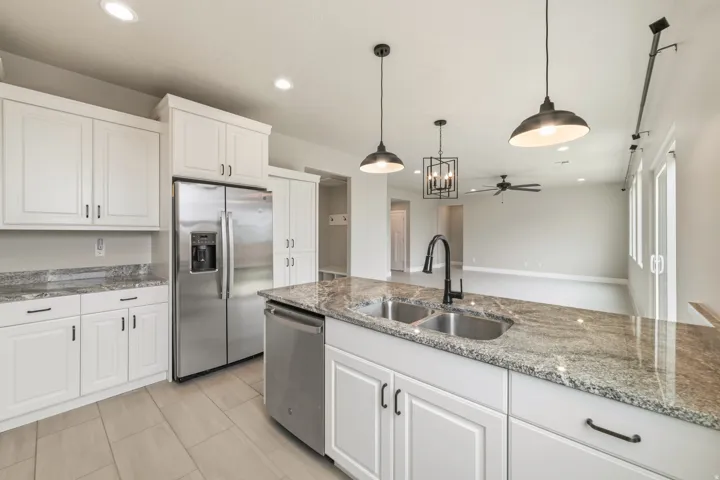 Kitchen featuring an island with dual basin sink and granite-style countertop, white shaker cabinetry with dark hardware, stainless steel refrigerator, and light tile flooring