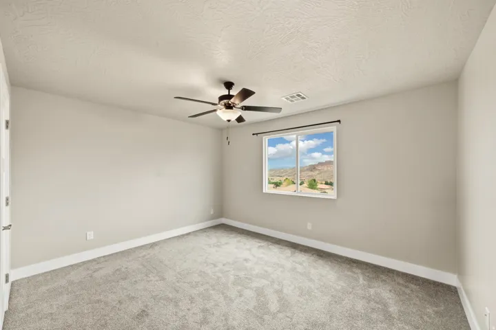 Spacious room featuring neutral paint, gray carpet, a ceiling fan with integrated lighting, and a large window offering expansive mountain scenery