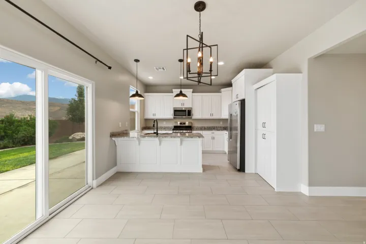 Open-concept kitchen featuring white cabinetry, granite countertops, stainless steel appliances, and a central island with pendant lighting