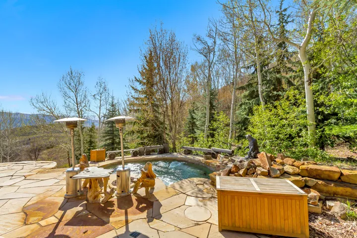 Outdoor hardscaping featuring a flagstone patio, a built-in spa, a stone retaining wall, and mature trees