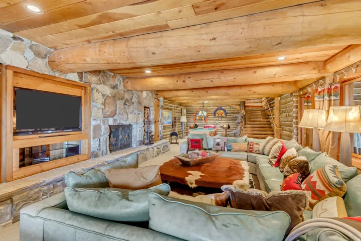 Spacious living area featuring exposed log beam ceilings, a stone fireplace, a built-in media console, stone accent walls, and recessed lighting