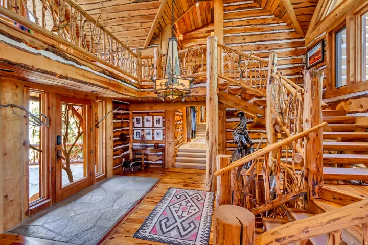 Grand foyer featuring natural log construction, a custom spiral staircase, a second-story overlook, wood-finish flooring, and a large decorative chandelier