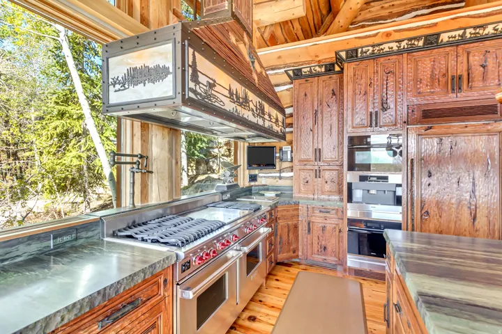 Gourmet kitchen featuring a large stainless steel range with griddle, custom metal range hood, wood-finish cabinetry, integrated paneled refrigerator, and stone countertops