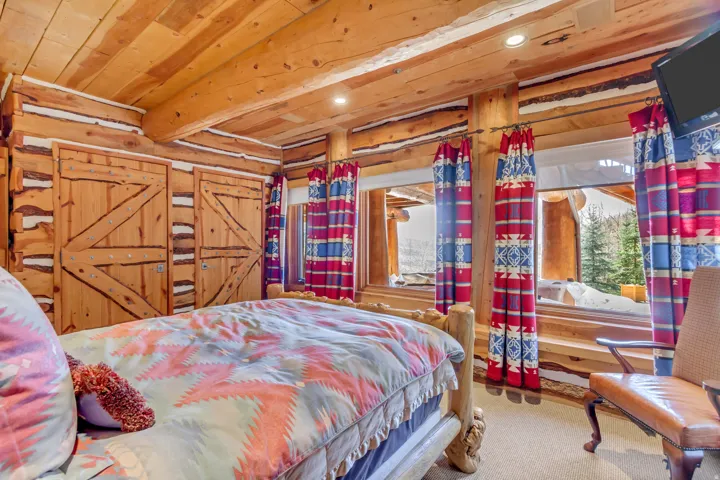 Rustic wood-paneled room featuring a built-in log bed frame, wood-finish ceiling, exposed log beams, and multiple windows