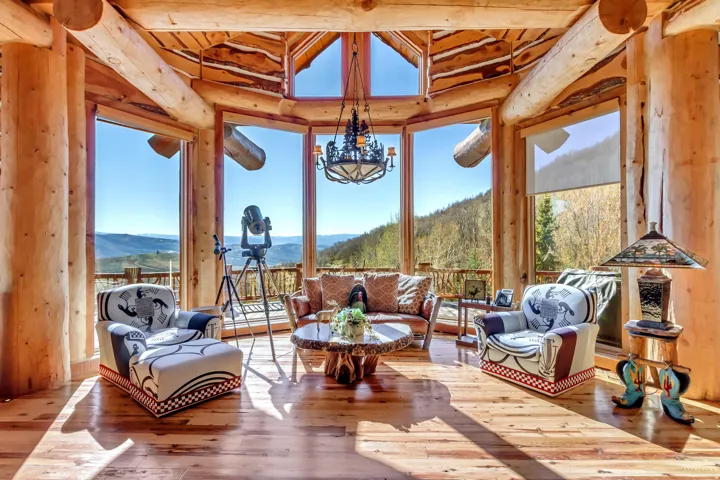 Great room featuring exposed log beam construction, wood-finish flooring, a vaulted ceiling, and expansive windows