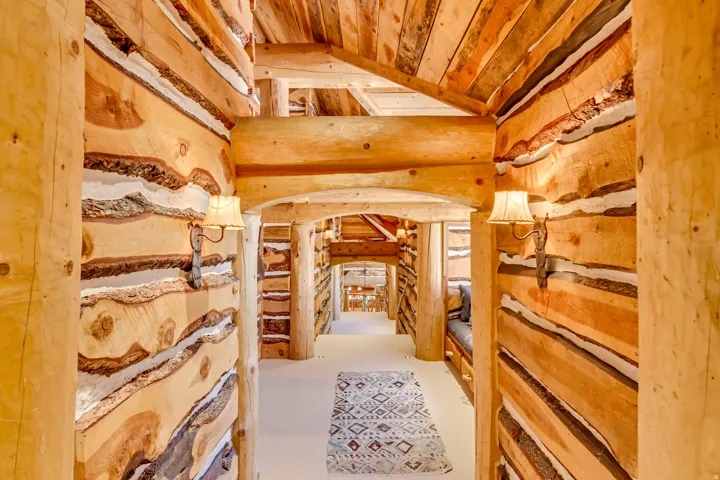 Rustic log construction hallway featuring exposed wooden beams, arched doorways, and built-in wall sconces