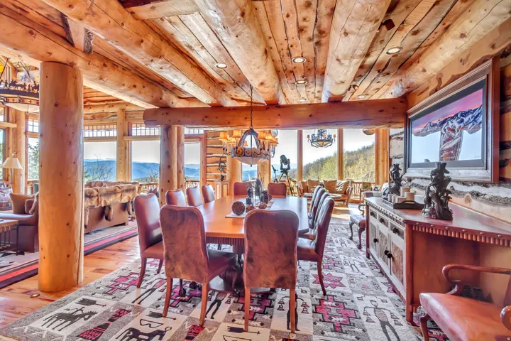 Dining area featuring expansive window placement, exposed log beam construction, wood-finish flooring, recessed lighting, and a prominent wood sideboard with integrated storage