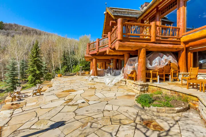 Expansive flagstone patio with natural stone steps, surrounded by mature evergreen trees and a backdrop of deciduous forest