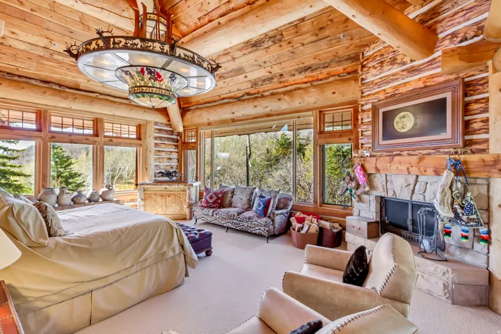 Expansive room featuring log walls and ceiling beams, a stone fireplace with a wood mantle, and multiple large windows