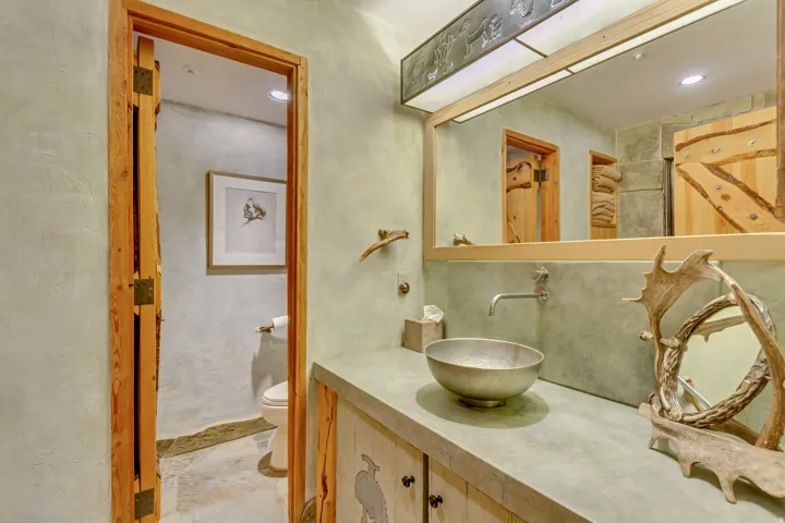 Bathroom featuring a vessel sink with wall-mounted faucet, wood-finish vanity with carved details, and a large mirror with integrated lighting