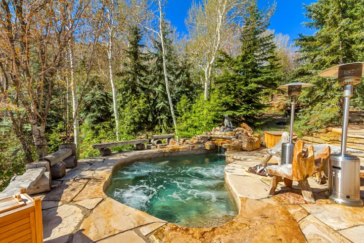 Custom-shaped spa featuring natural stone coping and a rock waterfall