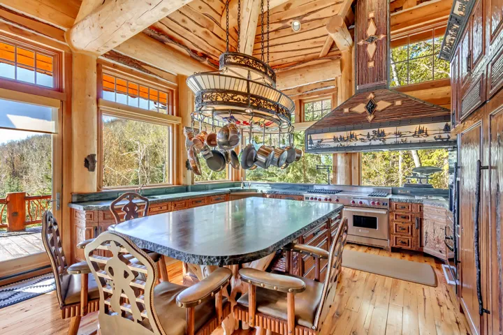 Gourmet kitchen featuring a large stone-top island, custom wood cabinetry, and a professional-grade range with a decorative hood
