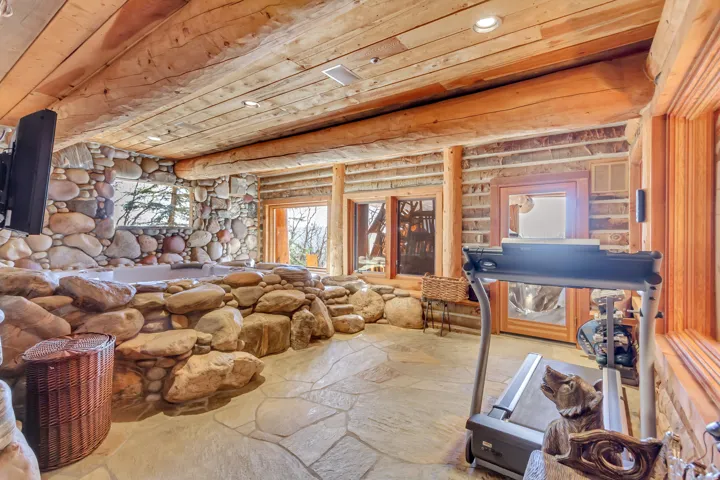 Stone-encased hot tub with flagstone flooring, wood-beamed ceiling, and exposed log walls