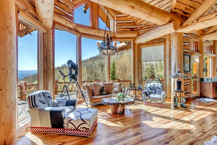 Great room featuring a cathedral ceiling, exposed log beams, expansive window walls, wood-finish flooring, and a wrought iron chandelier