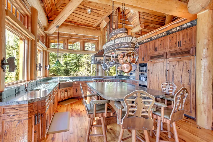 Rustic kitchen featuring extensive wood-finish cabinetry, an oversized stone-top island, a built-in pot rack, and integrated appliances