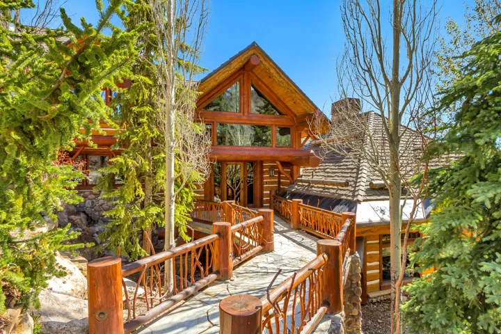 Log home exterior featuring a stone walkway, wooden railings, A-frame window design, and a rustic shingle roof