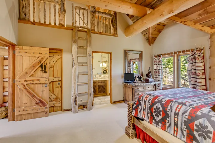 Vaulted ceiling with exposed wood beams and planking, custom wood barn doors, a built-in loft with log railing, and large windows