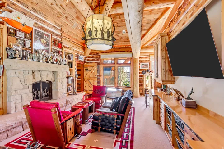 Spacious living area featuring exposed log walls and ceiling beams, a stone fireplace with a substantial hearth, built-in shelving, and a prominent built-in media console