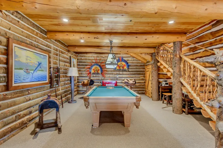 Spacious recreation area featuring a full-size billiard table, natural log walls, exposed beam ceiling, built-in recessed lighting, and a custom log staircase