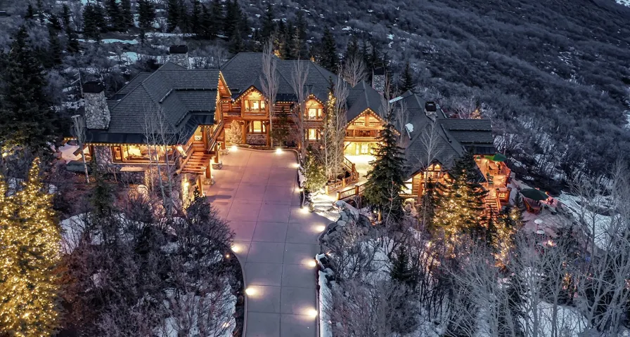 Expansive mountain-side property featuring multiple log-cabin style structures with stone chimneys and integrated outdoor lighting
