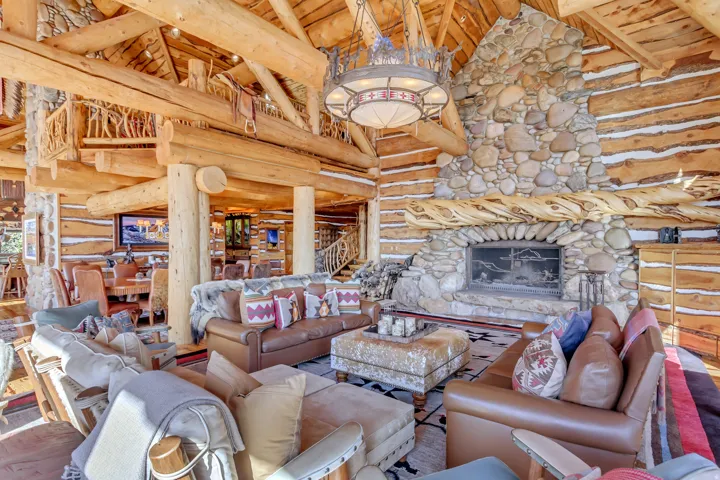 Expansive living space featuring a stone fireplace, exposed log walls, vaulted ceilings with exposed beams, a large chandelier, and a log staircase