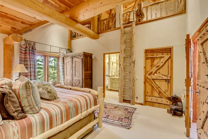 Room with exposed wood beams, a loft with a wooden ladder, and a window overlooking trees