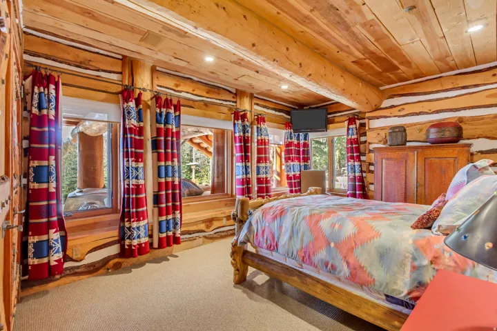 Log cabin interior featuring exposed wood-beam ceiling, wood-finish walls, recessed lighting, and carpeted flooring
