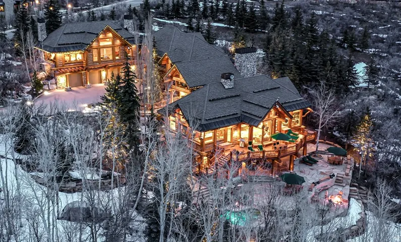 Expansive log home featuring multiple levels, extensive outdoor decking, and a distinct stone patio