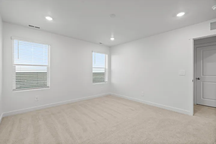 Carpeted interior space featuring two windows with horizontal blinds, recessed lighting, and a paneled interior door