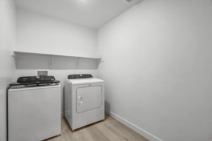 Laundry area with light wood-finish flooring, white walls, and built-in white shelving