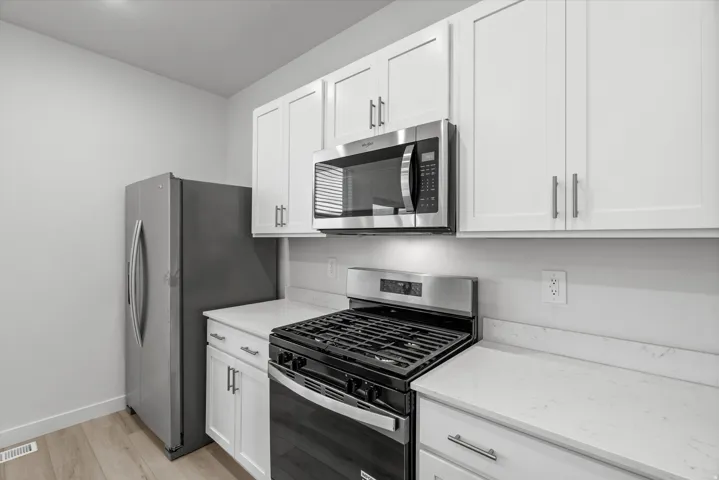 Modern kitchen featuring white shaker cabinetry, stainless steel appliances, quartz countertops, and wood-finish flooring