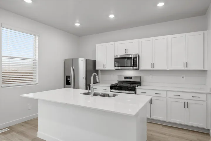 Modern kitchen featuring an island with an undermount double-basin sink, white shaker cabinetry, stainless steel appliances, and light wood-finish flooring