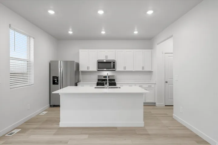 Contemporary kitchen featuring a center island with a stainless steel sink, white shaker cabinetry, stainless steel appliances, white subway tile backsplash, and wood-finish flooring