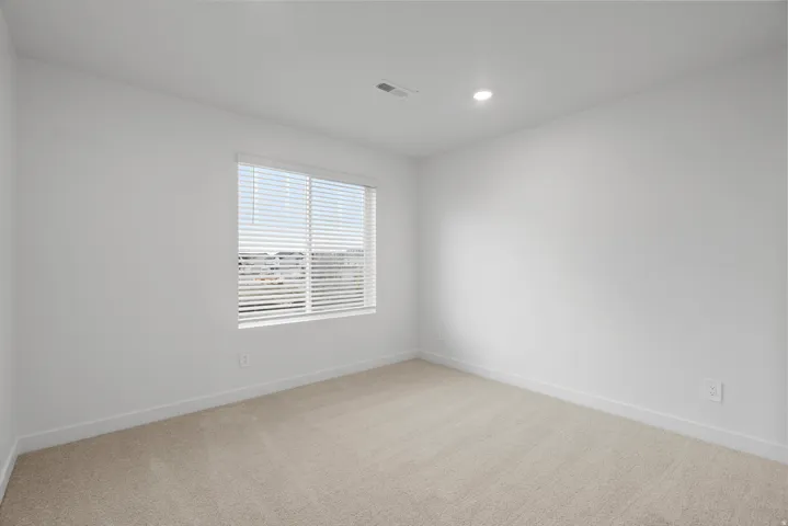 Carpeted room featuring white walls, a single window with horizontal blinds, and a recessed ceiling light