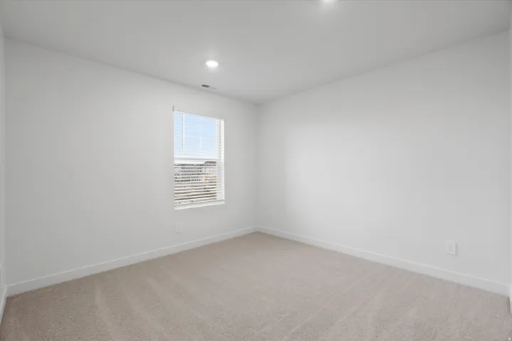 Neutral-toned wall-to-wall carpeting, white baseboards, and a single window with blinds