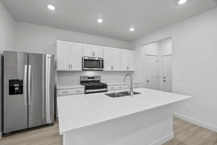 Kitchen featuring a large island with a double basin sink and gooseneck faucet, white shaker cabinetry, stainless steel appliances, and light wood-finish flooring