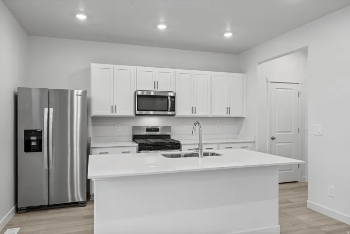 Kitchen featuring an island with a double basin sink, stainless steel appliances, white cabinetry, and light-toned wood-finish flooring