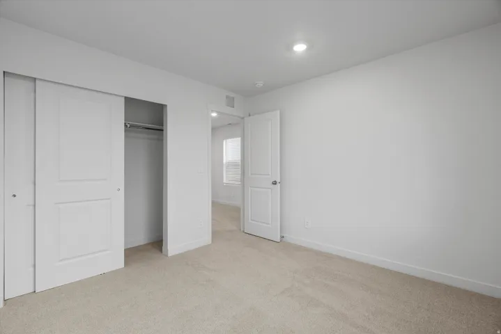Neutral-toned carpeted room featuring a white interior door, recessed lighting, and a closet with bi-fold doors and a hanging rod