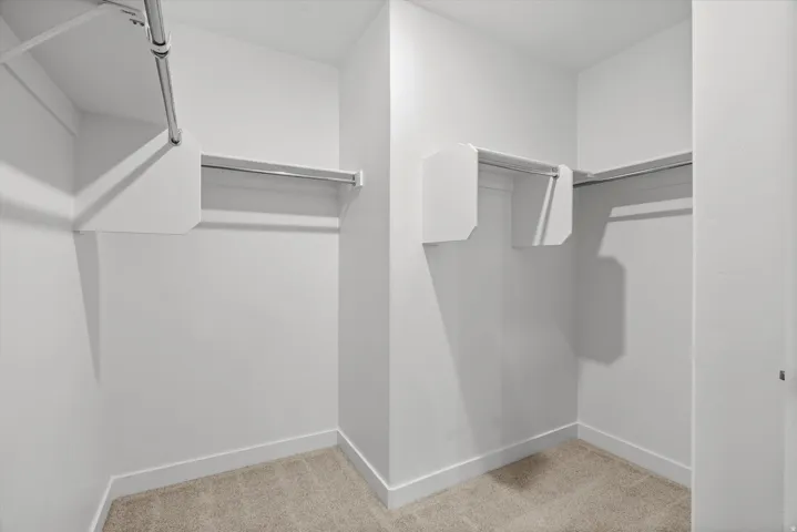 Walk-in closet featuring light-colored carpeting, white baseboards, and built-in white shelving with chrome hanging rods