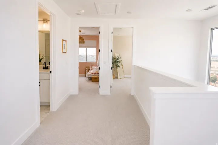 Bright hallway with neutral carpet flooring, white painted walls, and abundant natural light from large windows