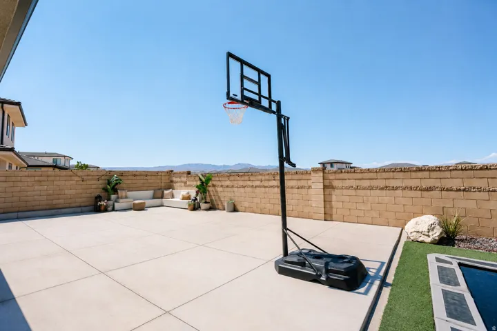 Expansive concrete patio with professional-grade basketball hoop, artificial turf lawn, and brick perimeter fencing